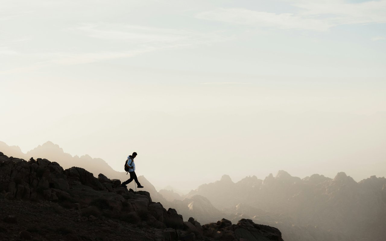 A backpacked hiker crosses a rocky ridge above hazy mountain peaks.