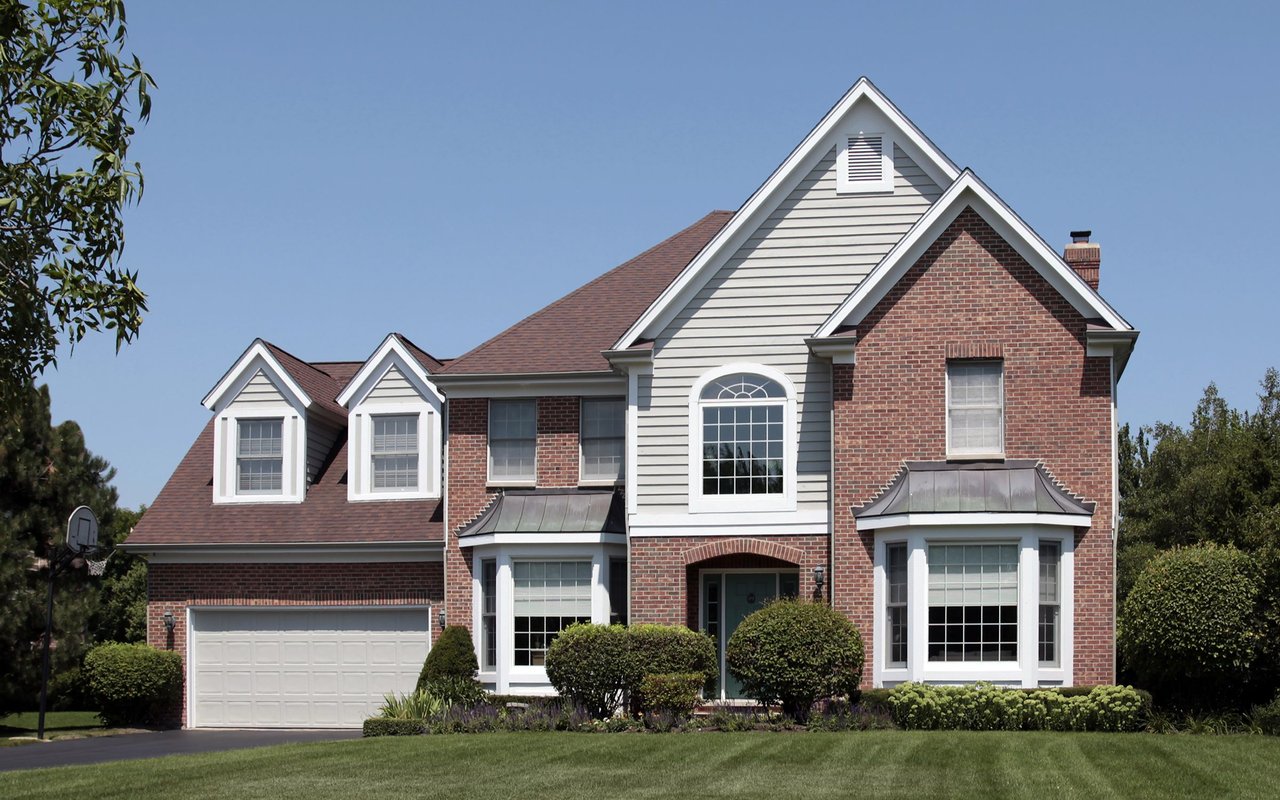 Two-story brick and gray-sided house with gabled dormers, a two-car garage, and a broad lawn.
