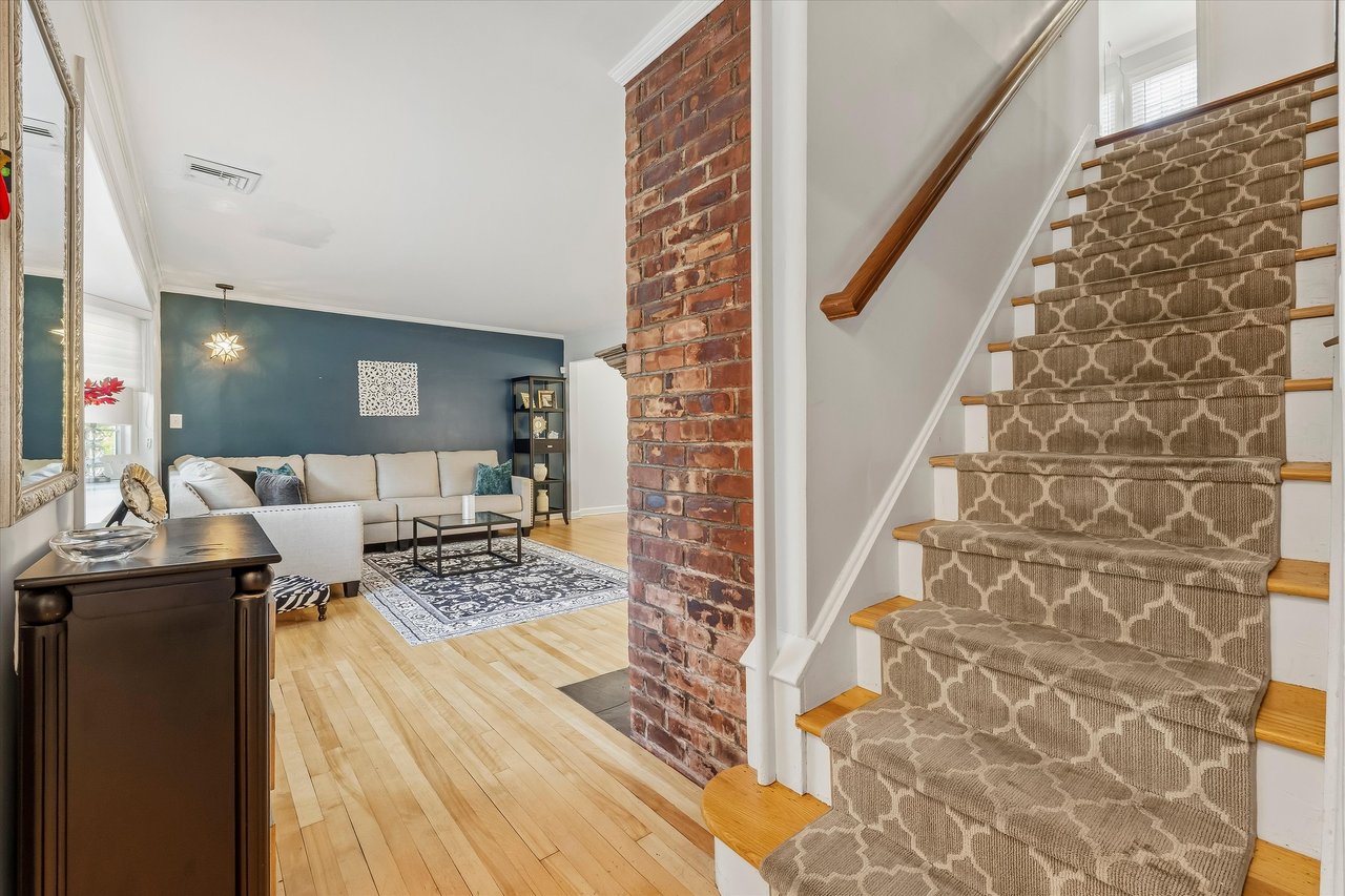 Living room beside a carpeted staircase, with a brick column and cream sectional sofa.