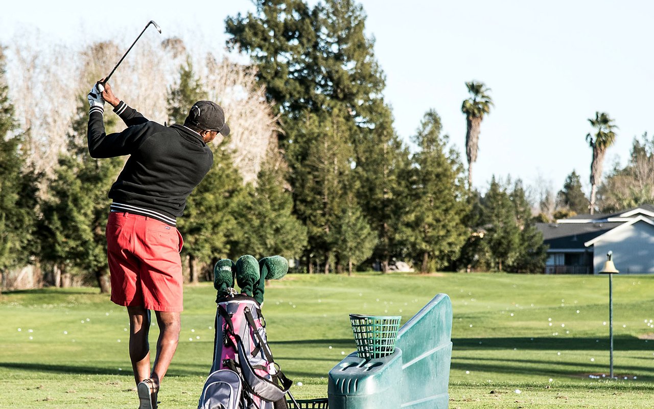 Golfer practicing on a sunny course beside a golf bag and practice equipment.