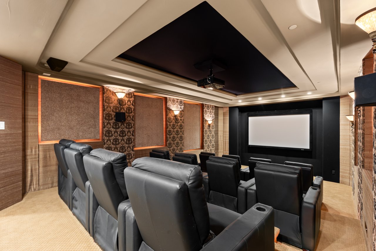Home theater with rows of black leather recliners facing a large projection screen.
