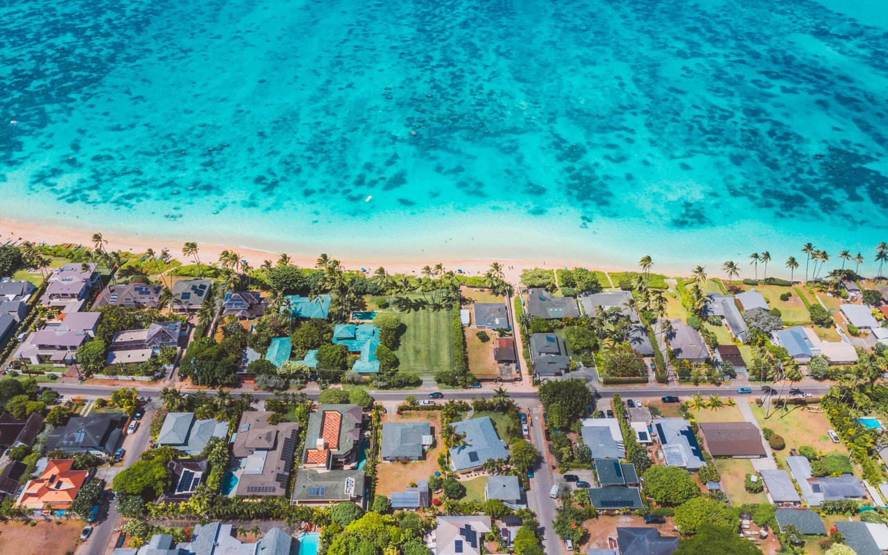 Aerial view of beachfront homes and palm trees beside turquoise water in Kawailoa Kailua.