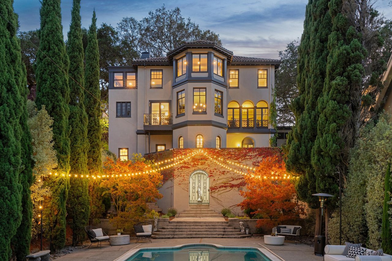 Mediterranean-style home framed by cypress trees, with a lit entry courtyard and swimming pool.