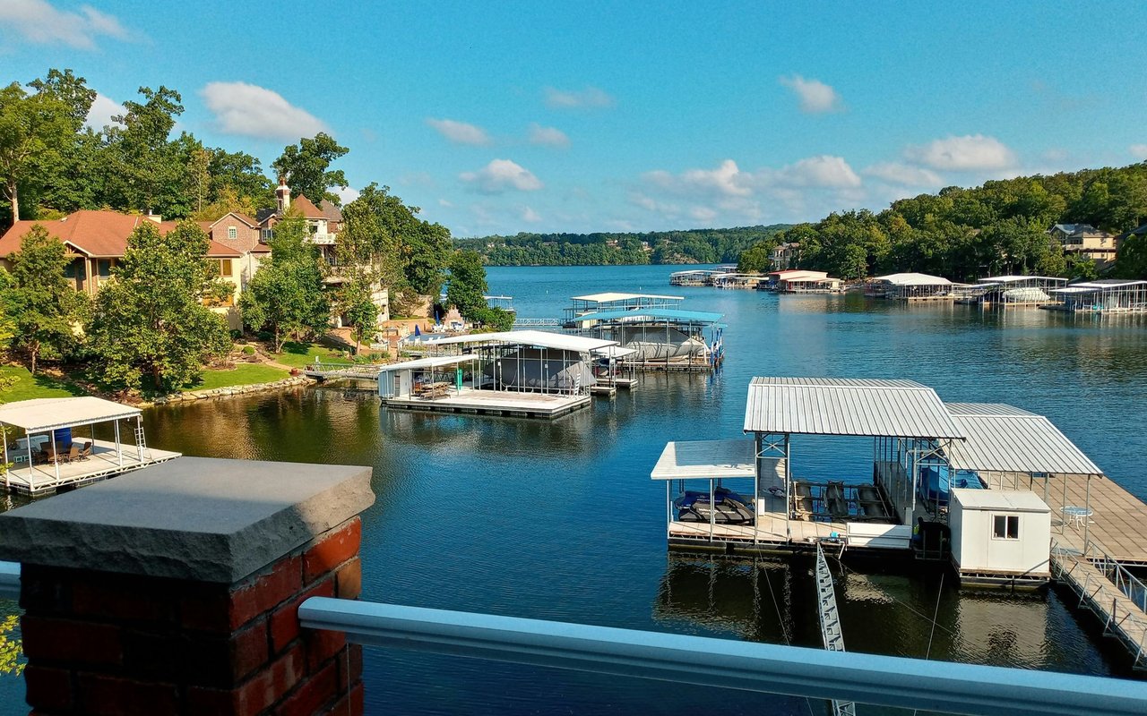 Lakefront homes and covered boat docks line a blue lake bordered by wooded hills.