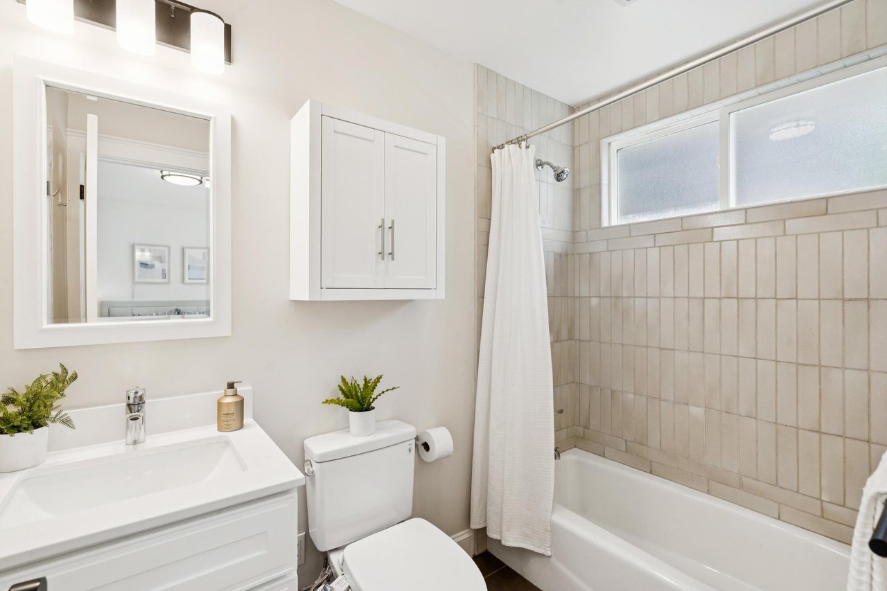 Bathroom with a white vanity and tub, tiled surround, and frosted window.