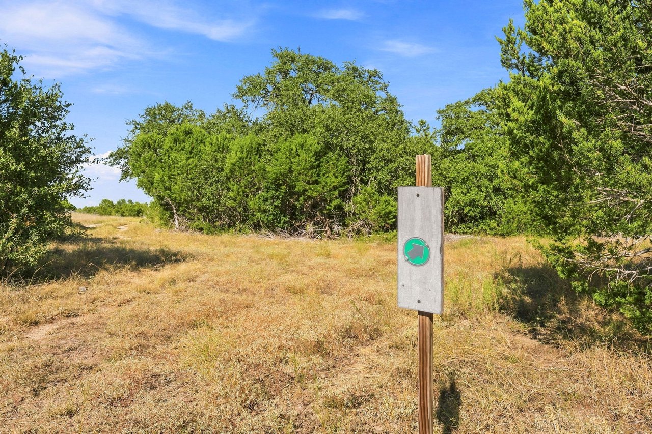 Grassy ranch path bordered by trees, with a green right-pointing arrow sign.