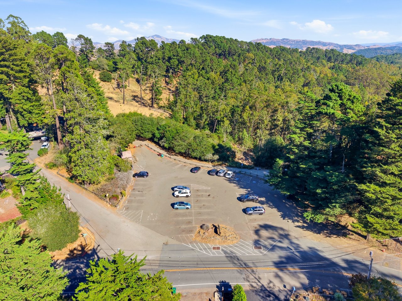 Aerial view of a parking lot beside a wooded hillside, with distant mountain ridges.