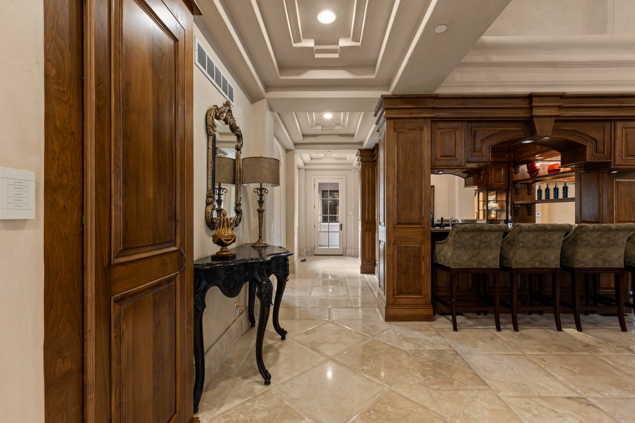 Foyer leading to a dark wood kitchen bar with upholstered stools and a carved console table.