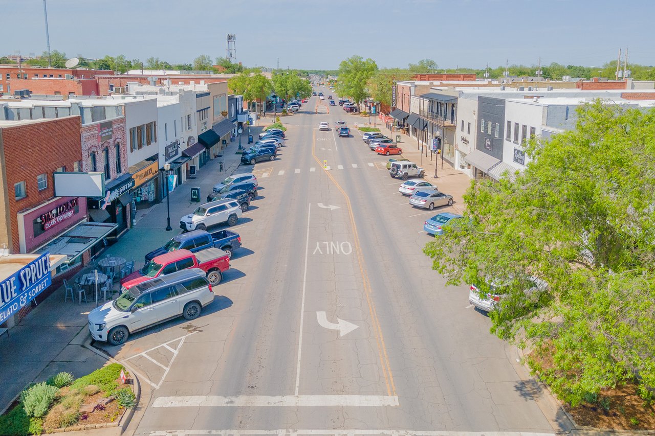 Aerial view of a small-town main street lined with shops, parked cars, and leafy trees.