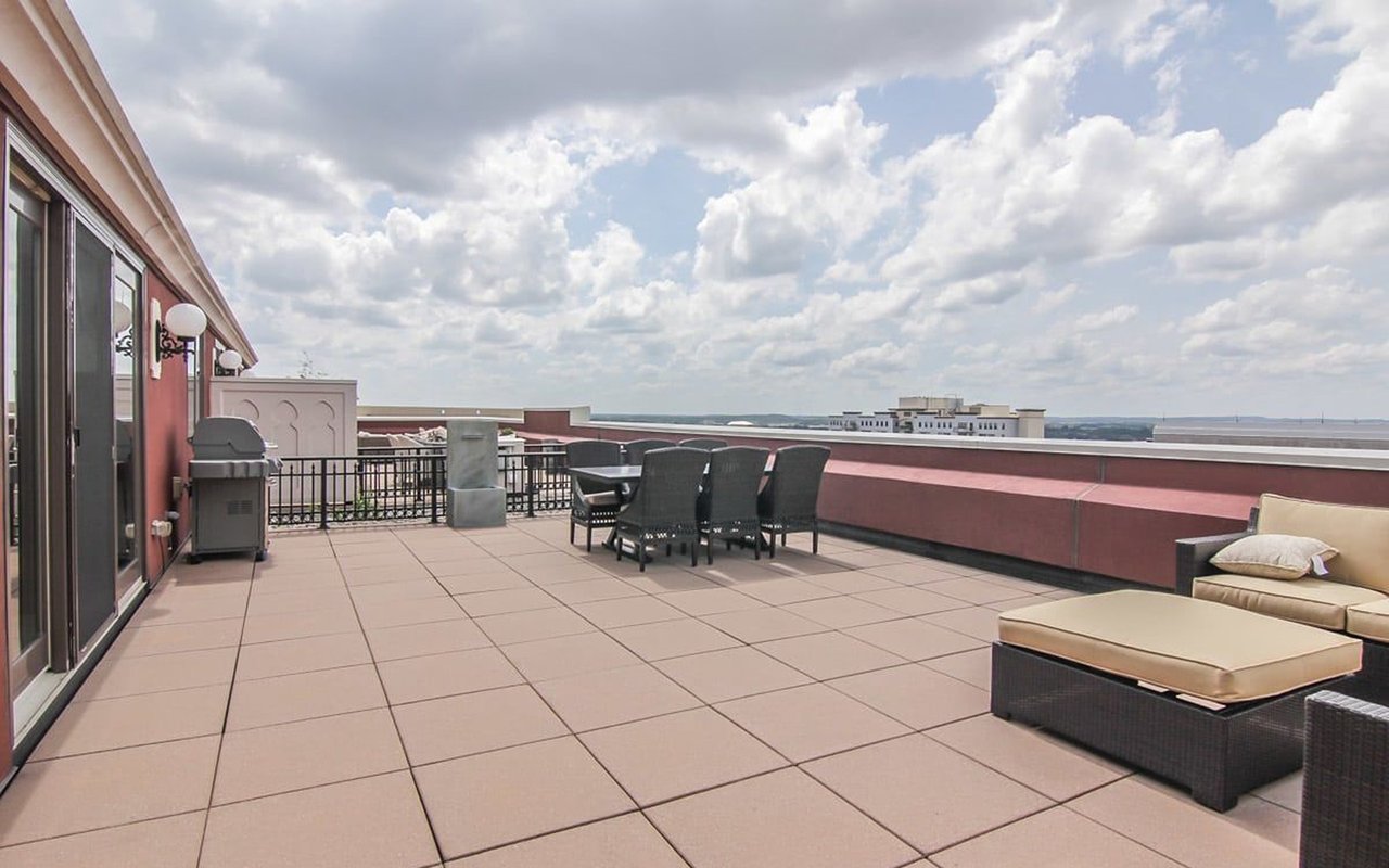 Rooftop terrace with tiled paving, wicker lounge seating, and distant city views.