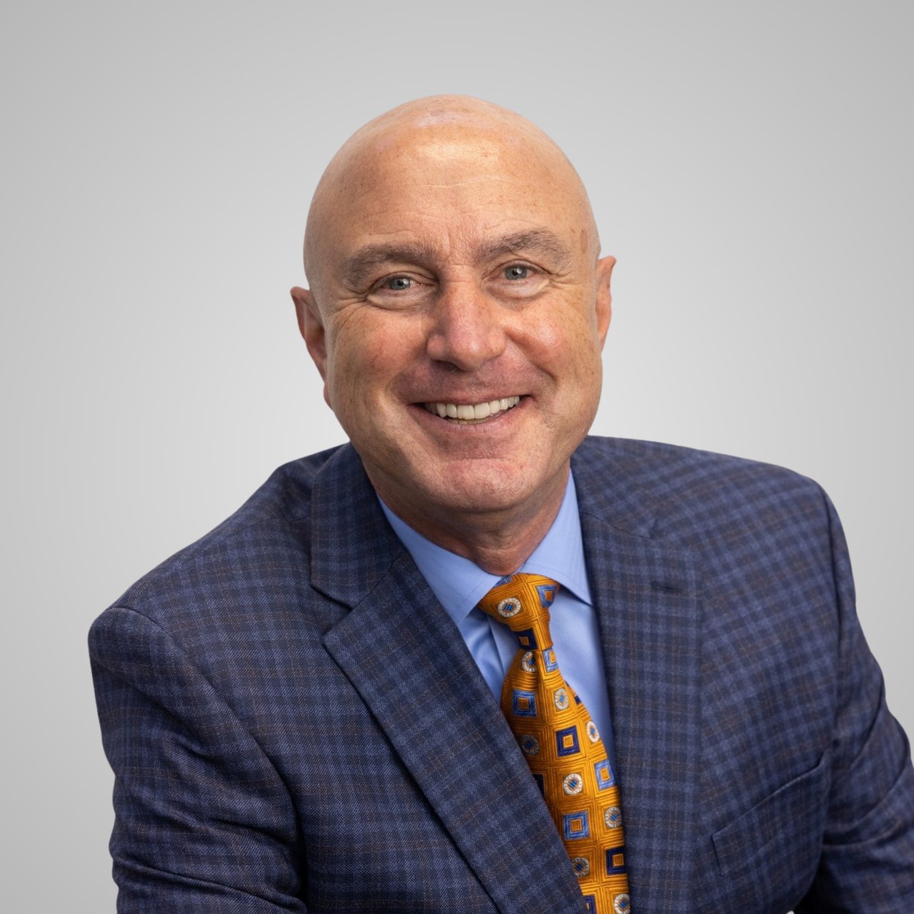 John Kay, smiling in a blue checked suit and gold patterned tie