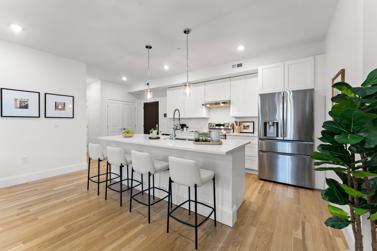 Modern white kitchen with a large island, seating, stainless steel appliances, and light hardwood floors.