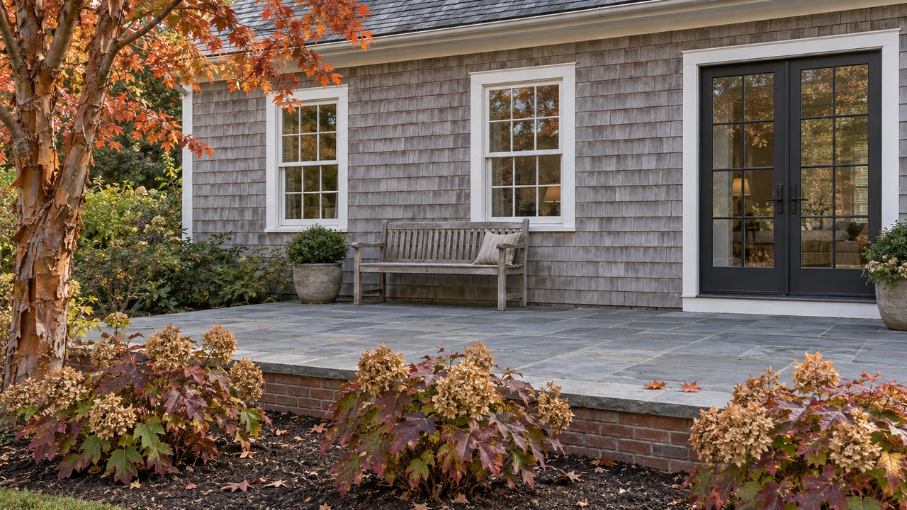 Cedar-shingled home overlooking a bluestone terrace, weathered teak bench and burgundy oakleaf hydrangeas beneath a paperbark maple.