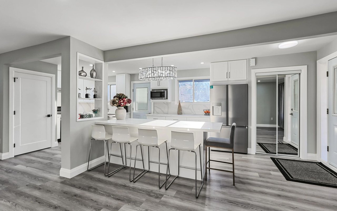 Renovated white kitchen with a large island, four bar stools, stainless steel appliances, and gray flooring.