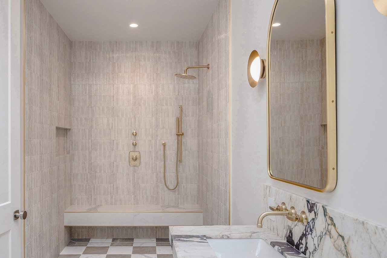 Bathroom with a tiled walk-in shower, built-in bench, brass fixtures, and marble vanity.