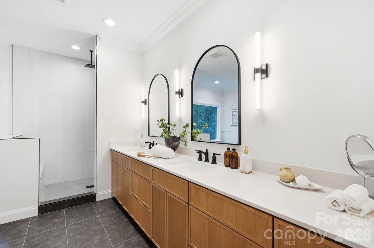 Modern bathroom with a long wood double vanity, arched mirrors, and glass-enclosed shower.