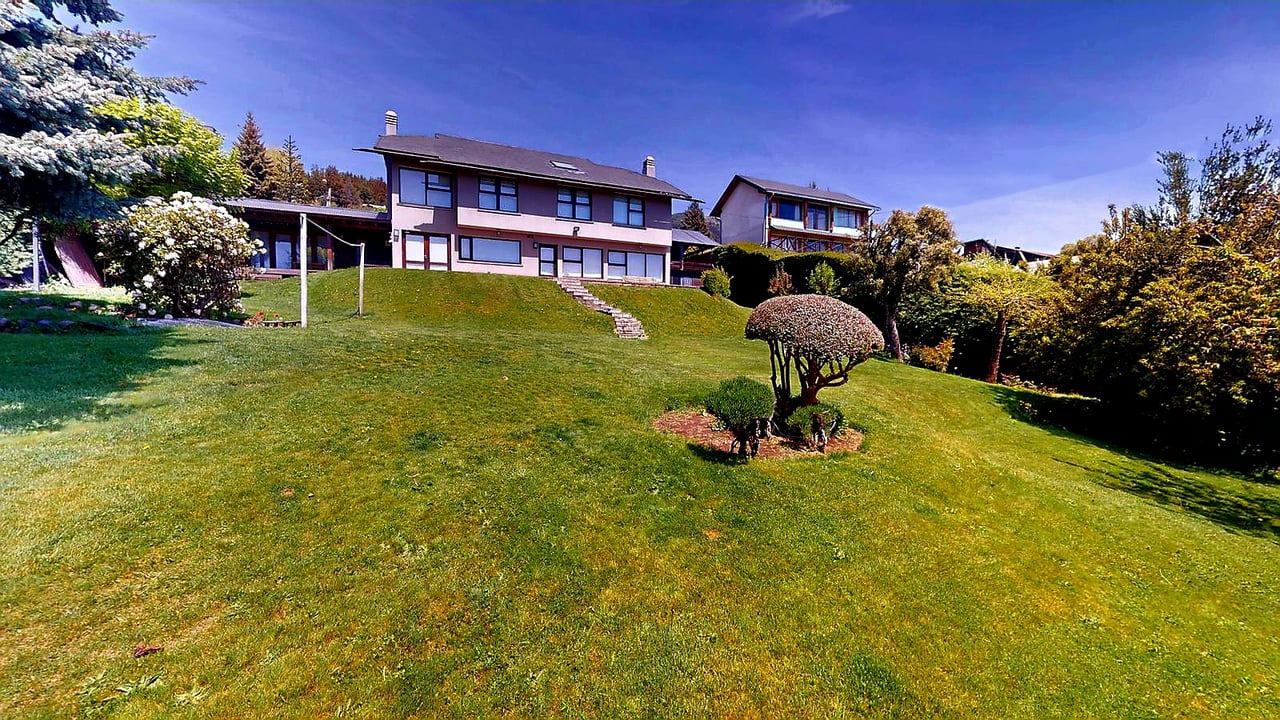 Two-story house above a sloping lawn, with garden steps, shaped shrubs, and mature trees.