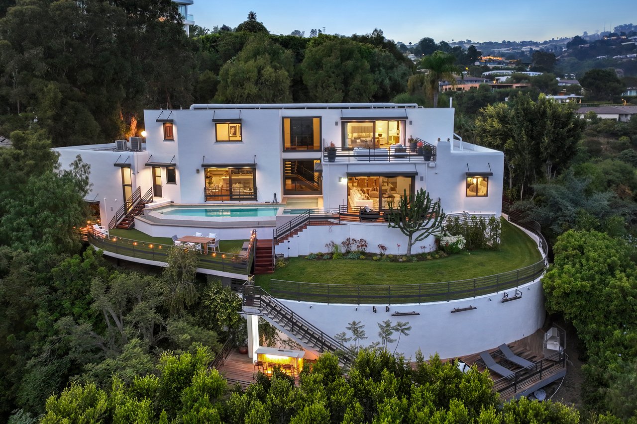 Modern hillside home with a swimming pool and curved lawn, photographed at dusk.