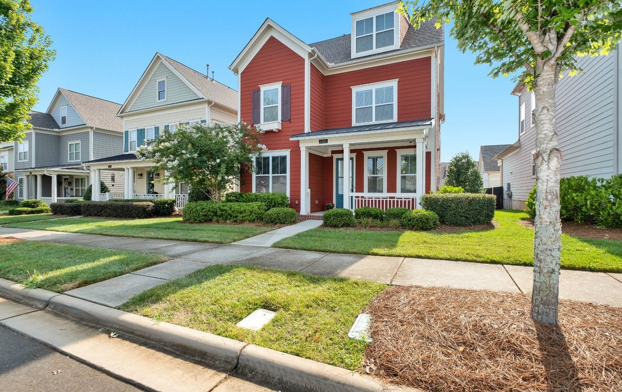  A sunny, eye-level street view shows a vibrant red two-story house with white trim, a dark blue front door, 