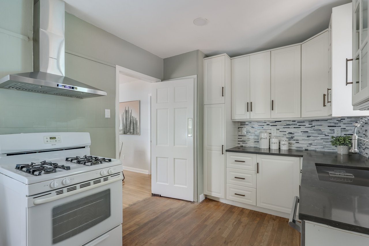Kitchen with white shaker cabinets, mosaic tile backsplash, dark counters, and a white gas stove.