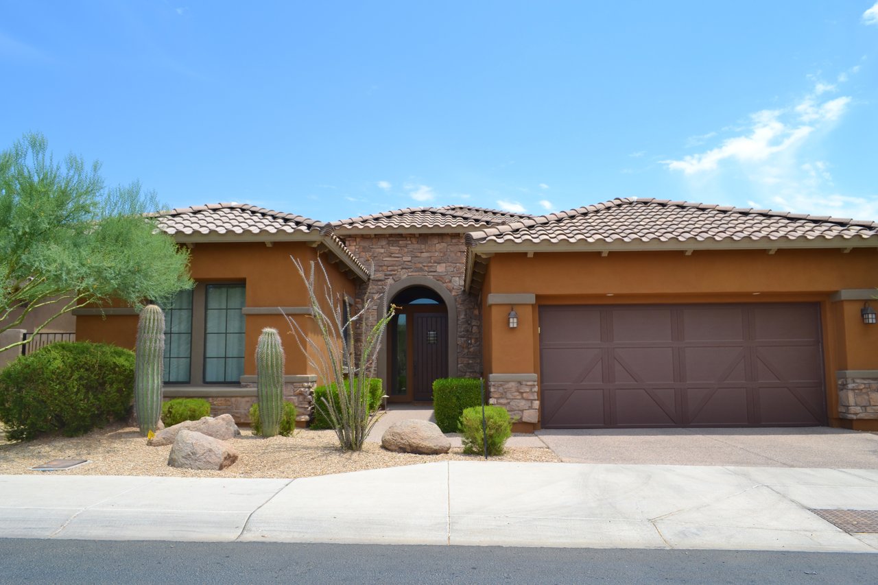 Single-story stucco home with a stone entry, double garage, and desert landscaping.