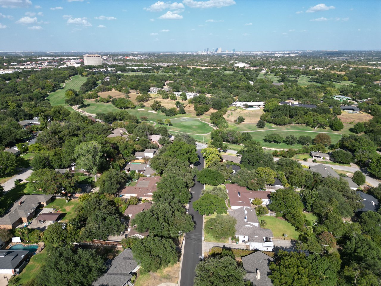 Aerial view of a leafy neighborhood and golf course, with the Fort Worth skyline in the distance.
