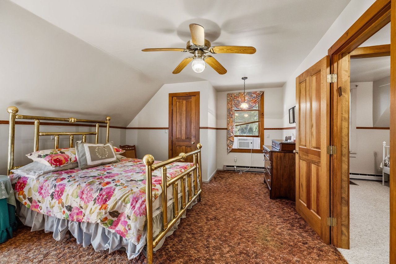 Bedroom with a brass bed, floral bedding, brown carpet, and an open wooden door.