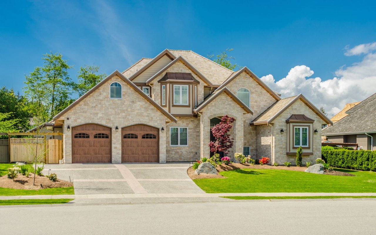 Two-story stone house with twin garage doors, a broad driveway, and landscaped lawn.