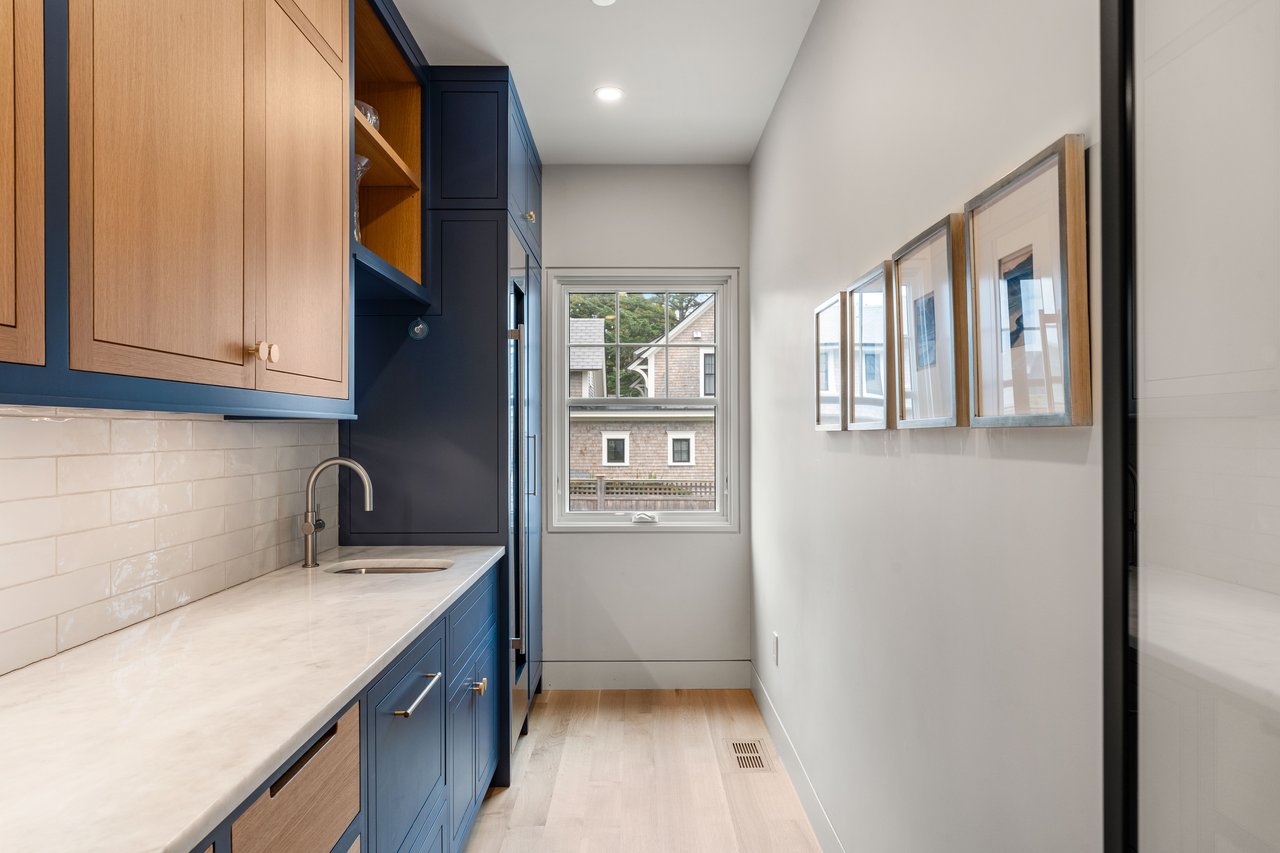 Narrow kitchen with blue and wood cabinetry, light counters, and a window overlooking a neighboring house.