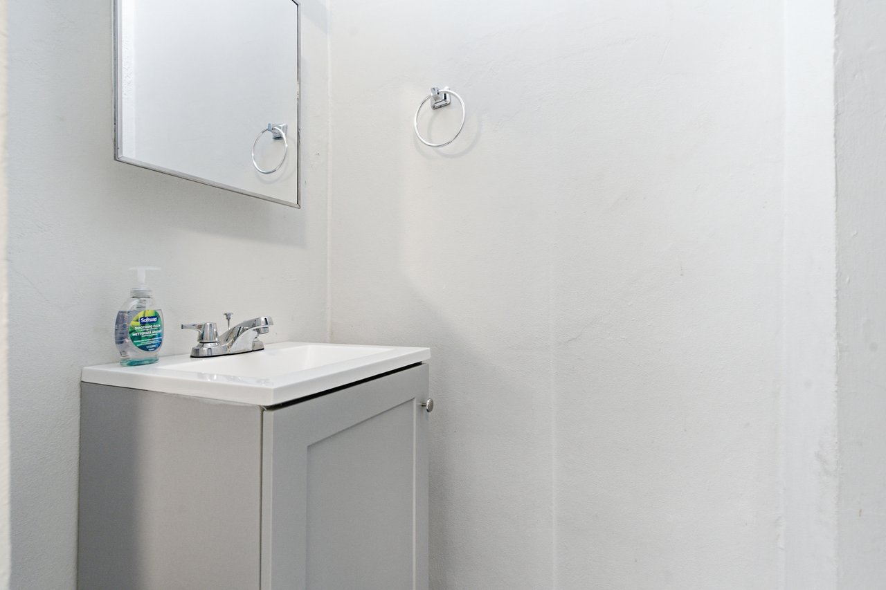 Bathroom vanity with a white sink, gray cabinet, chrome faucet, and wall mirror.