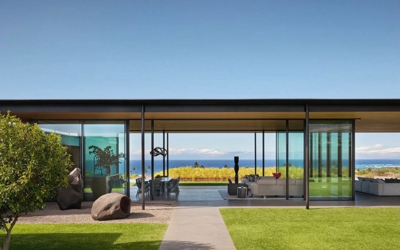 Modern glass-walled coastal home with a furnished patio and ocean views
