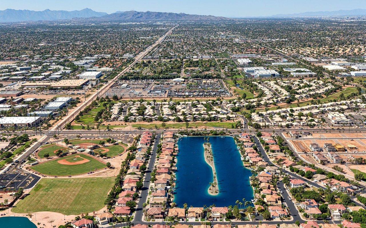 Aerial view of a suburban community with a long lake, baseball fields, and distant mountains.