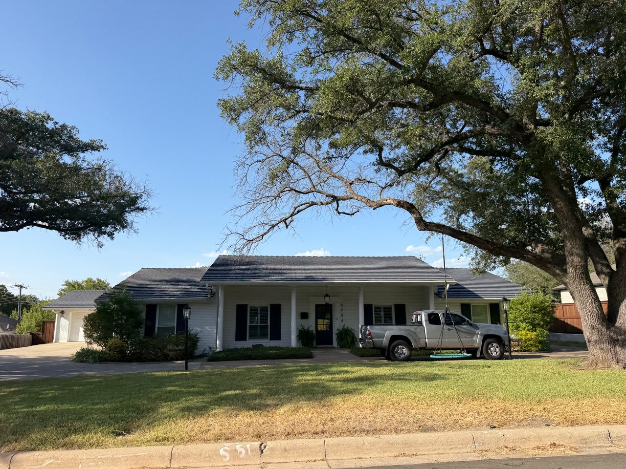 Single-story ranch home beneath a large oak tree, with a silver pickup parked in the driveway.