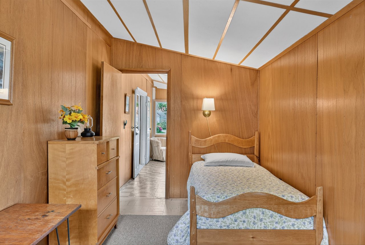 Wood-paneled bedroom with a single wooden bed and dresser beside an open doorway.
