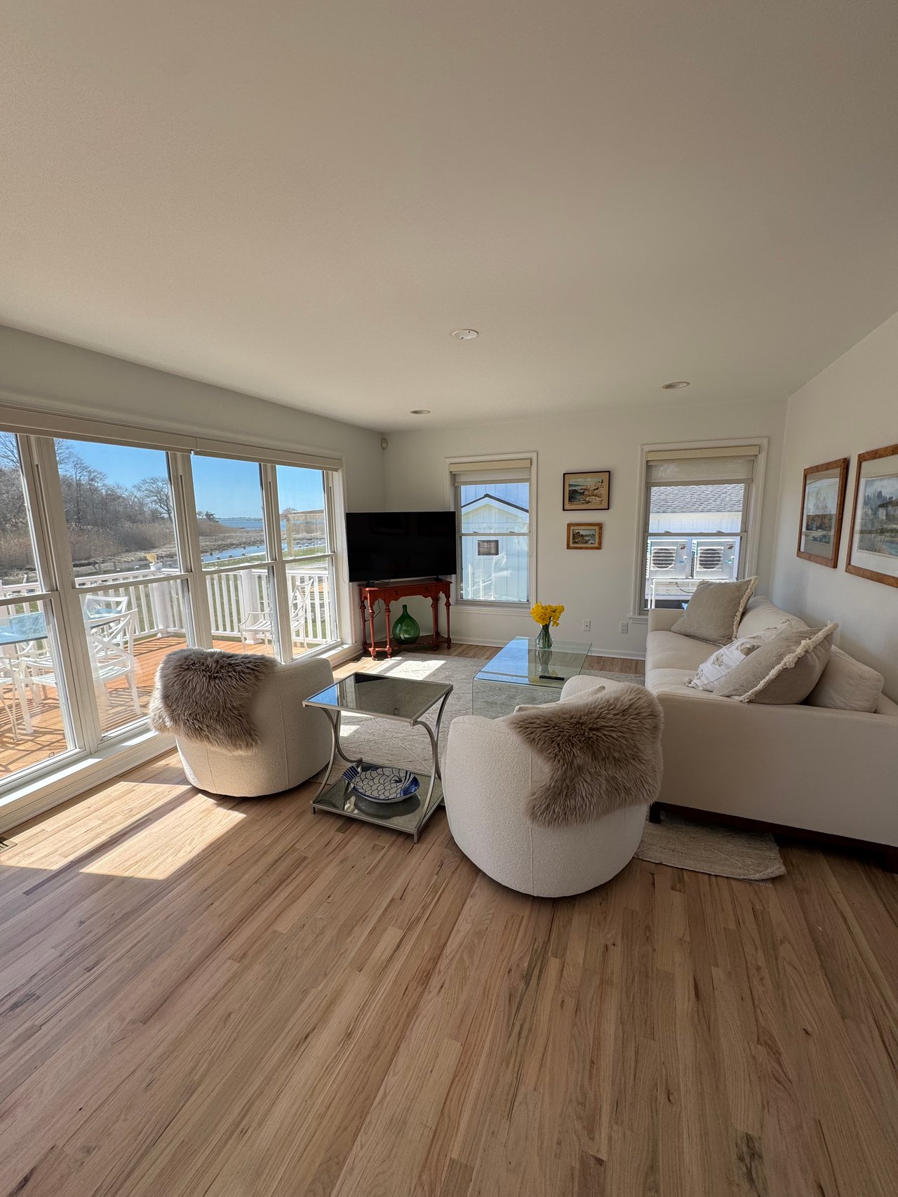 Living room with cream seating and hardwood floors, looking through large windows toward the water.