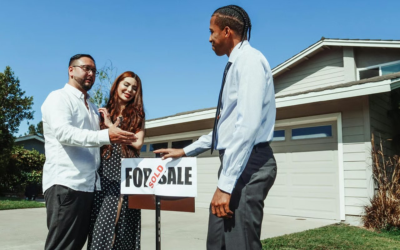 Single-story home with a couple and agent beside a SOLD sign.