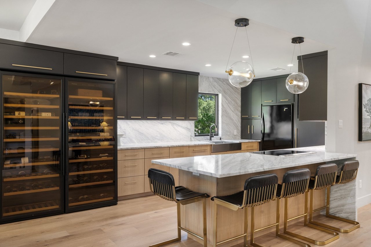 Modern kitchen with a marble island, dark cabinetry, and two glass-front wine refrigerators.