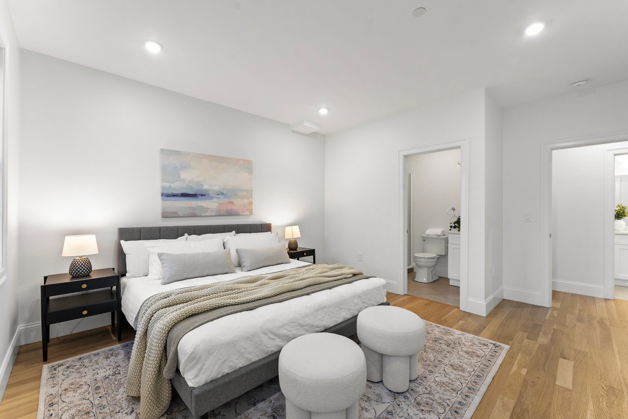 Furnished bedroom with a gray upholstered bed, patterned rug, and two round stools at the foot.