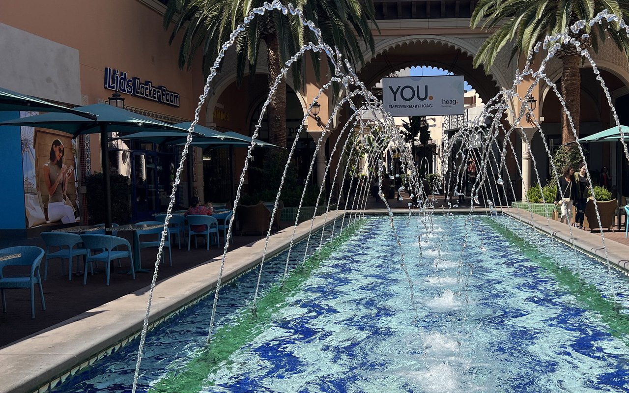 Fountain jets arcing over the tiled reflecting pool at Irvine Spectrum Center, palms and arcades behind