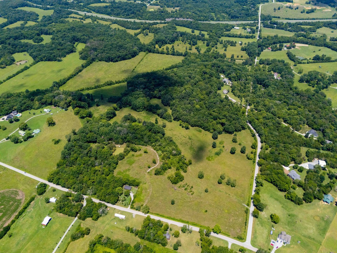 Aerial view of rolling green acreage with wooded areas, scattered homes, and roads.