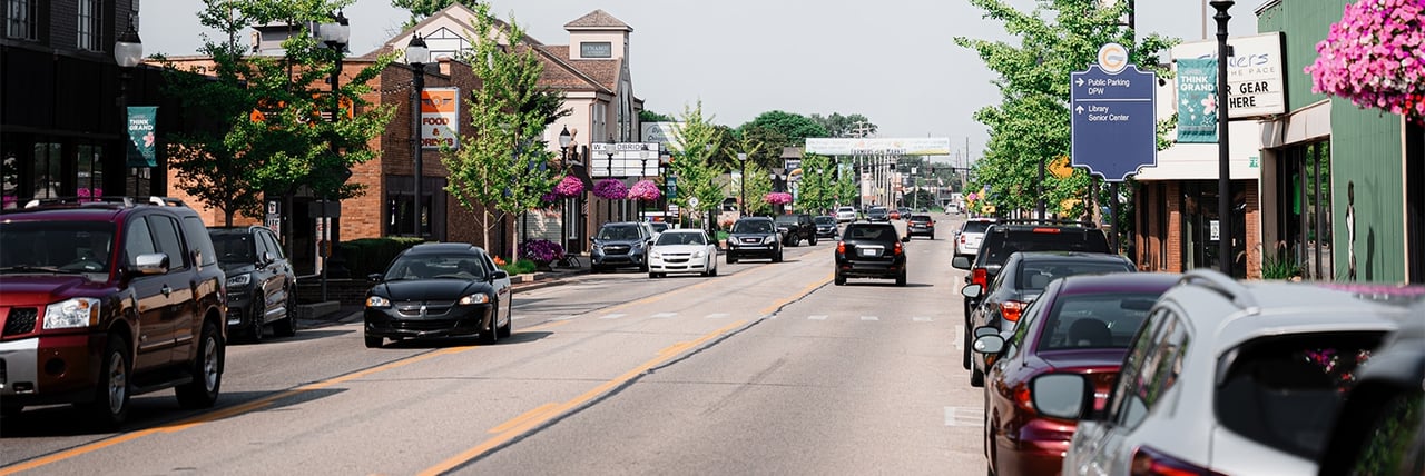 Downtown Grandville Michigan street with shops, cars, and hanging flower baskets along the sidewalks.