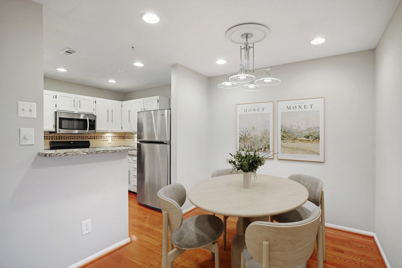Dining area with a round table beside a white kitchen with stainless steel appliances.