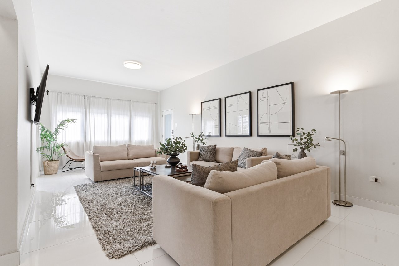 Living room with beige sofas, a coffee table, textured rug, and framed abstract artwork.
