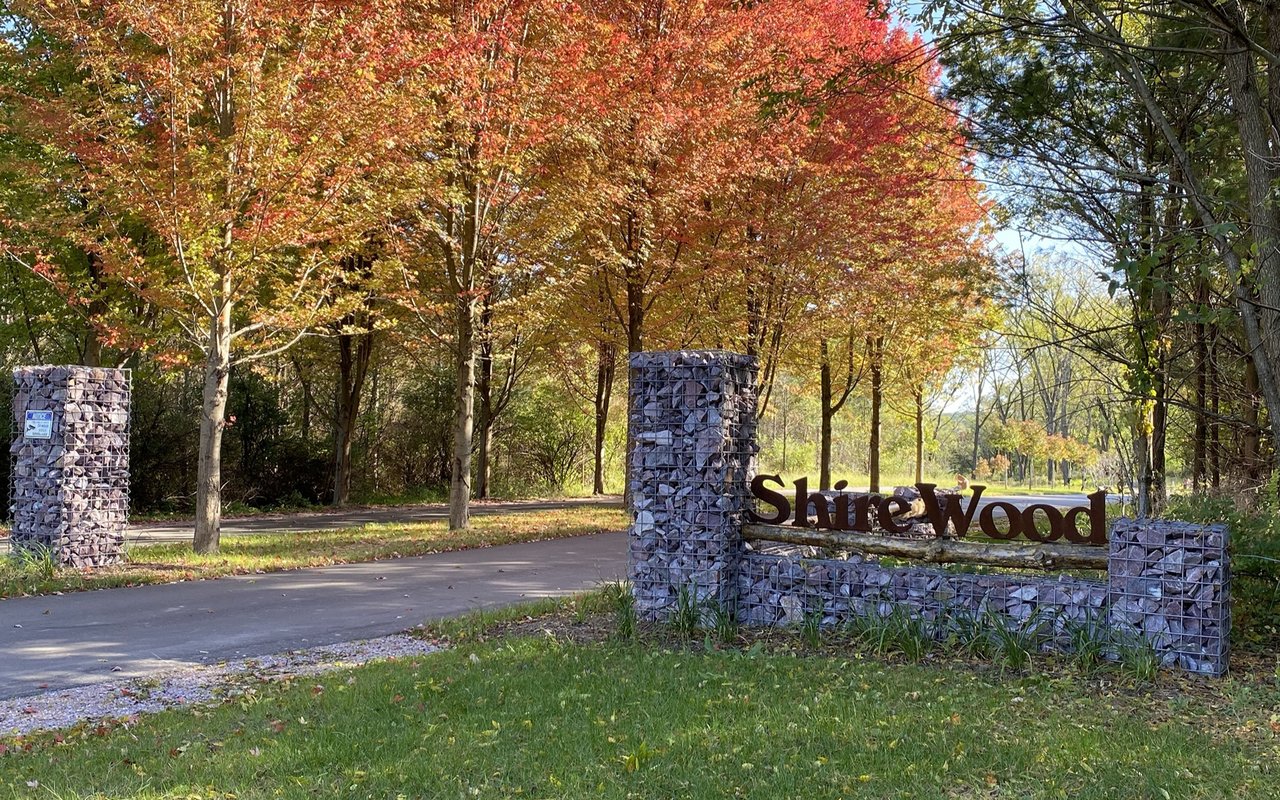 Shire Wood entrance sign beside a road, framed by stone pillars and autumn trees.