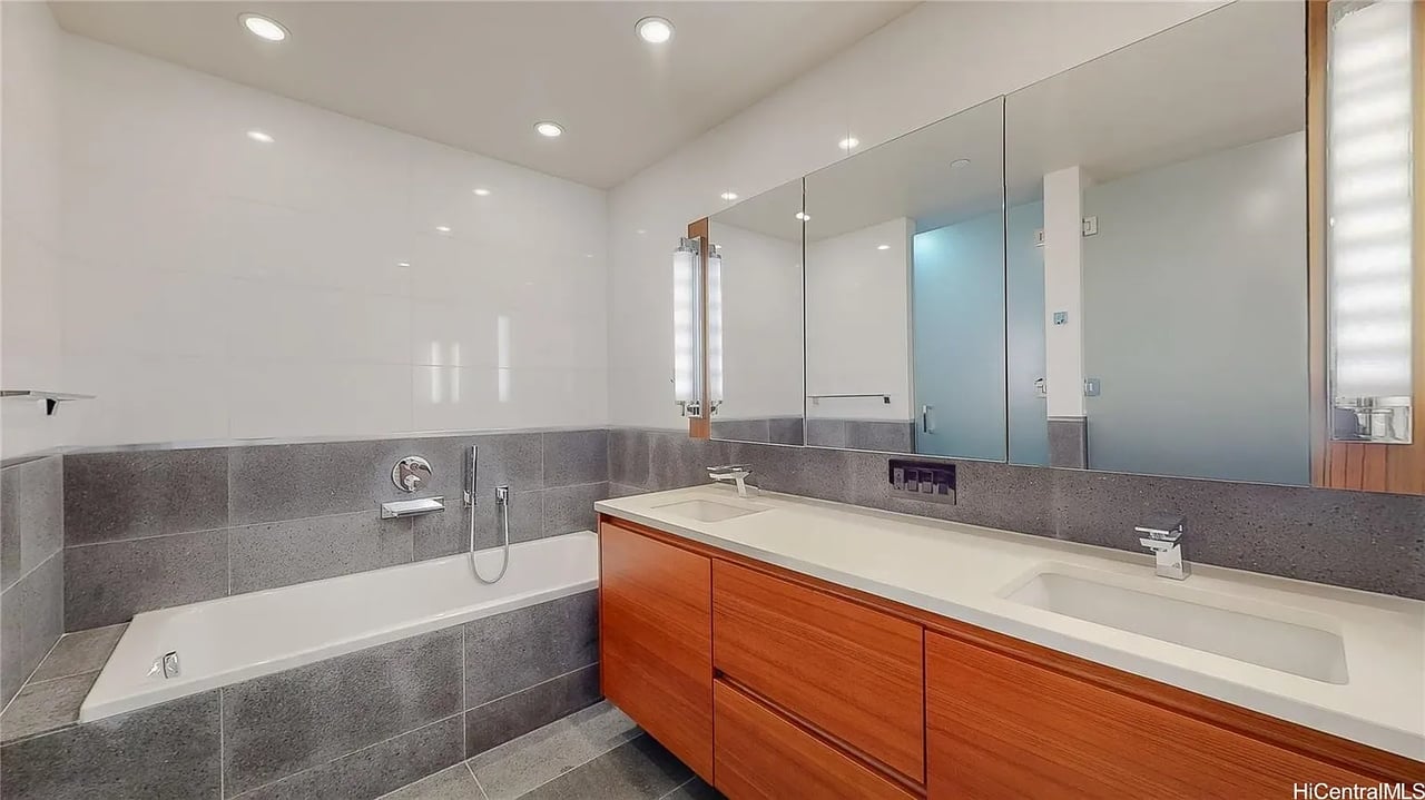 Modern bathroom with a built-in tub, gray tile, and a long double-sink wood vanity.