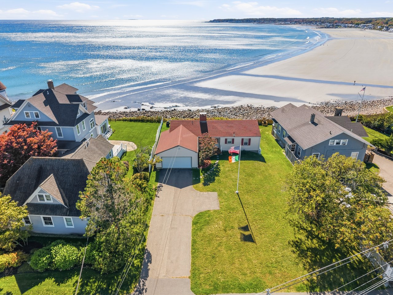Aerial view of coastal homes beside a broad sandy beach and blue ocean.