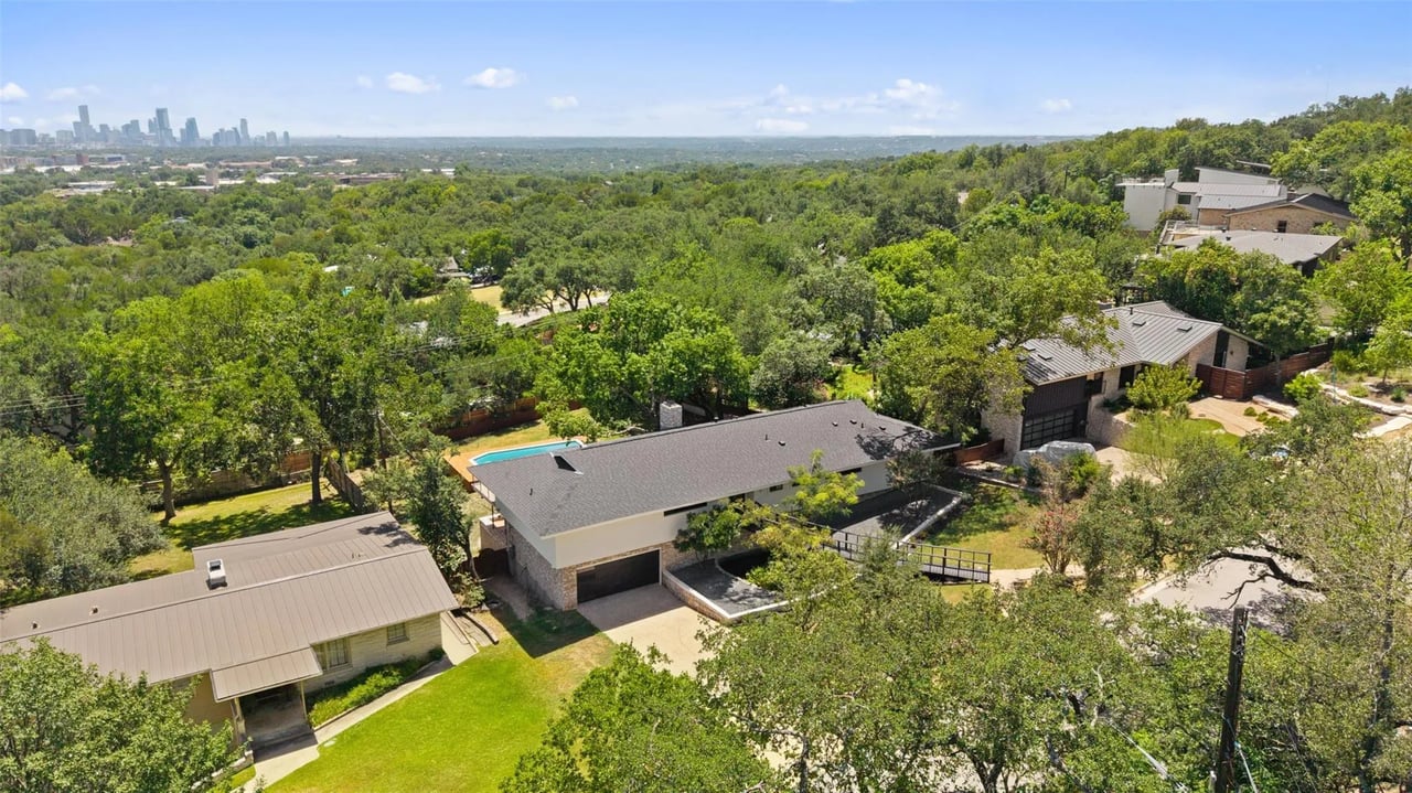 Aerial view of homes among mature trees, with the Austin skyline in the distance.