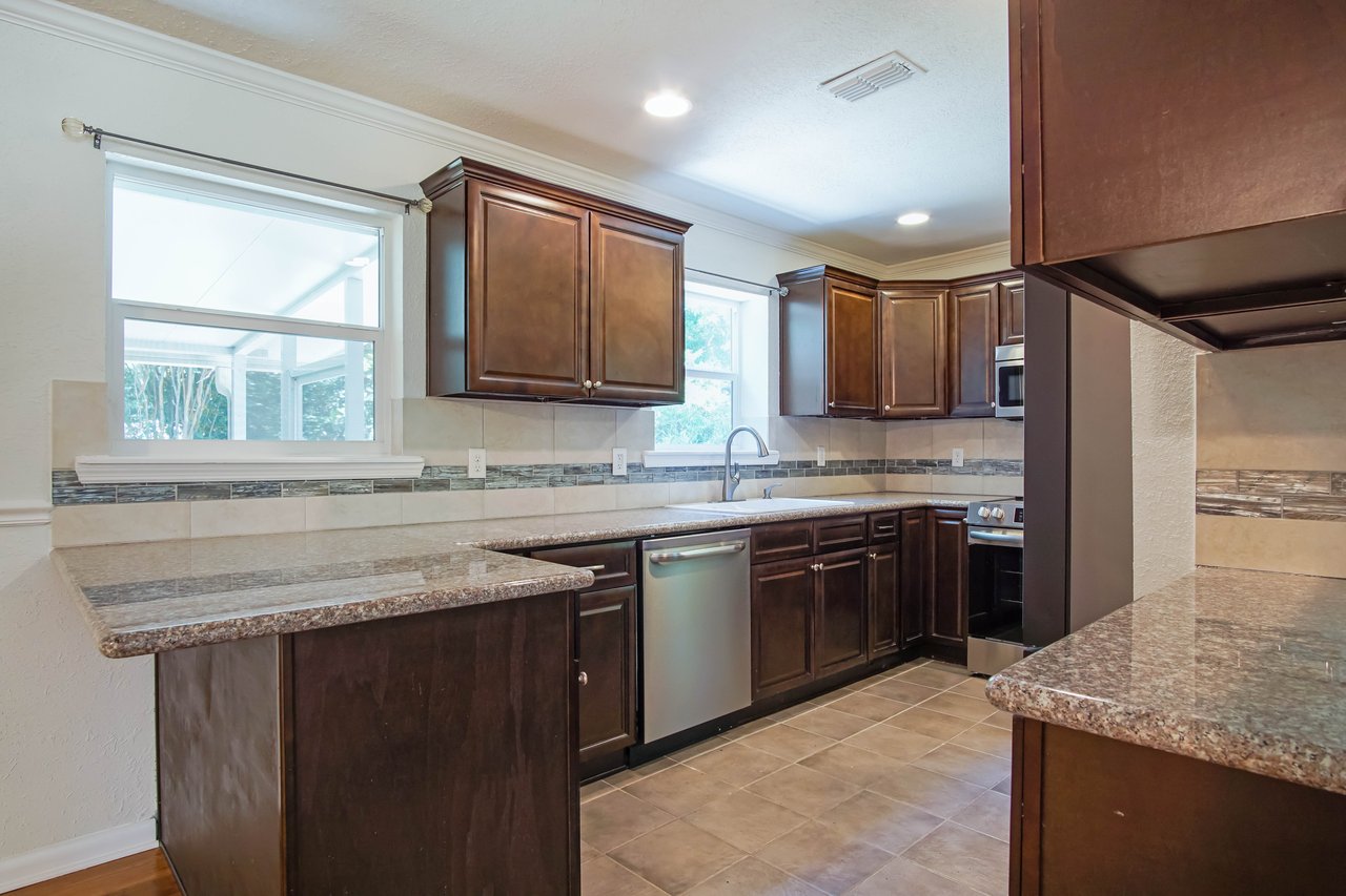 Spacious kitchen with dark wood cabinets, granite countertops, and stainless steel appliances. Sunlight streams through a window, creating a cozy ambiance.