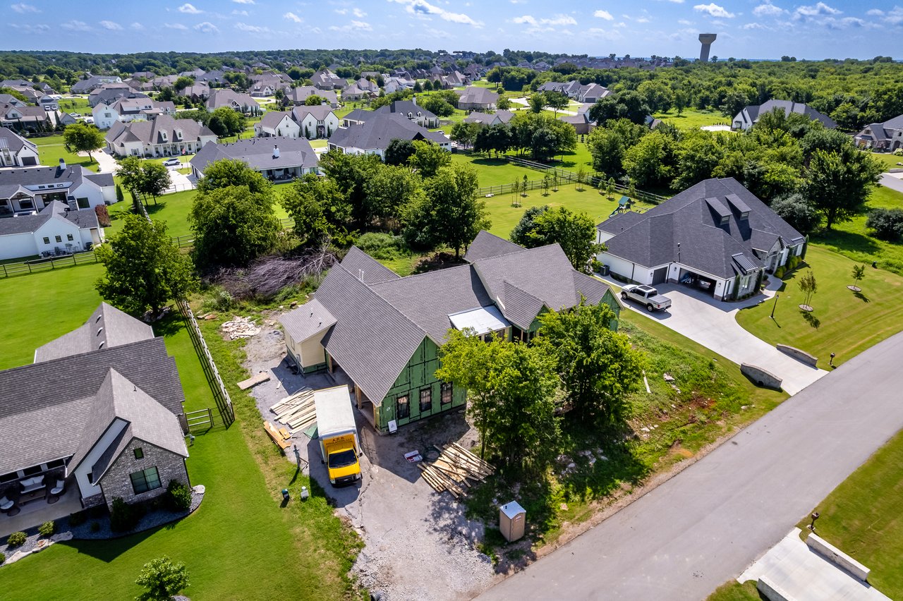 Aerial view of a partially built house with exposed framing and a work truck among finished suburban homes.