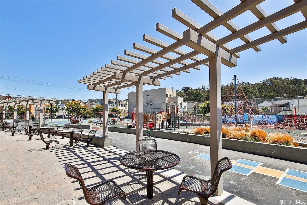 Neighborhood park plaza with a wooden pergola, outdoor seating, and a playground.